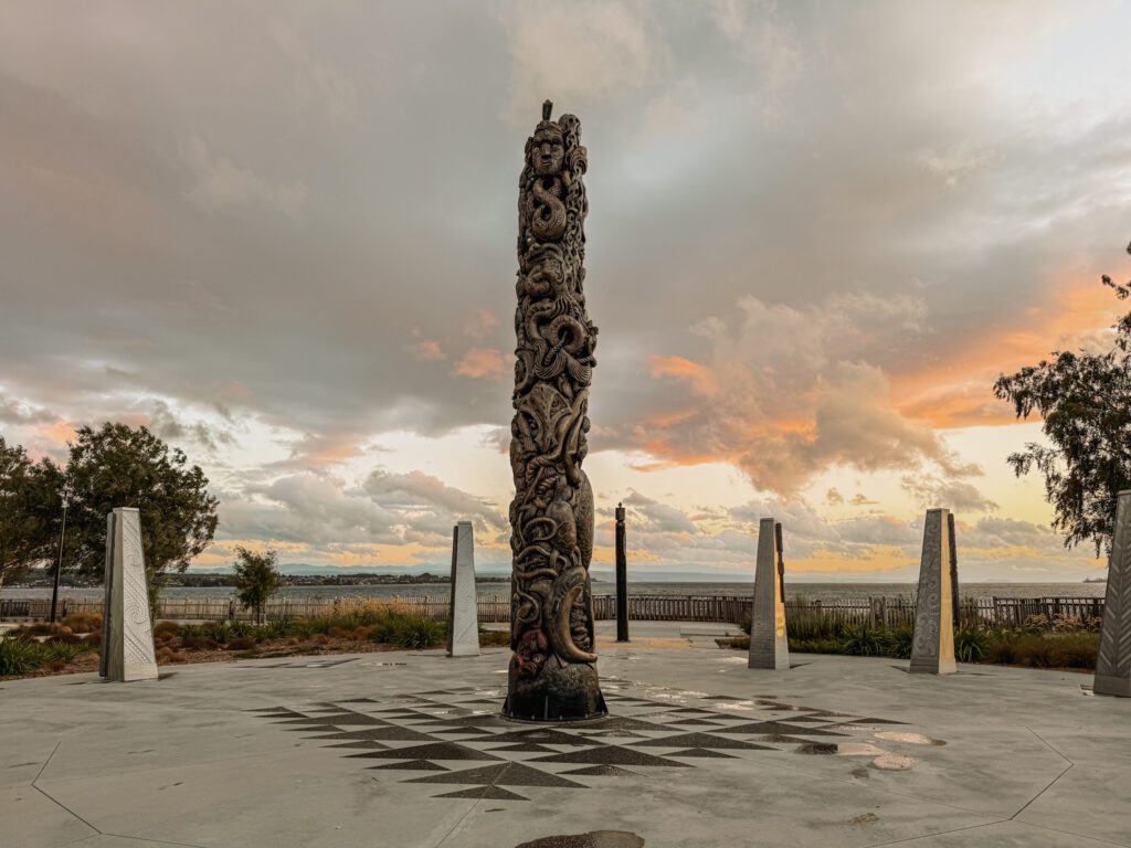 A tall carved wooden trunk in front of a sunset in Taupo