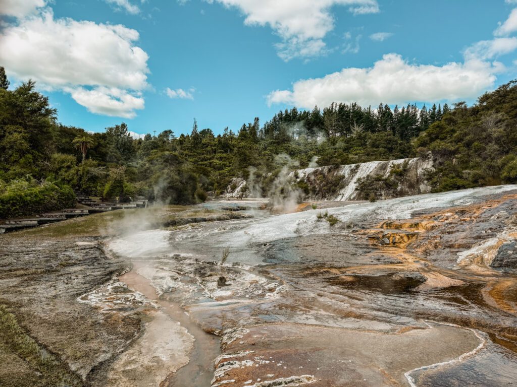 A geothermal landscape with smoke rising from the ground and orange swirls in Taupo