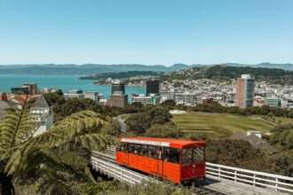 A red cable car going up a hill with a bay in the background - Wellington itinerary