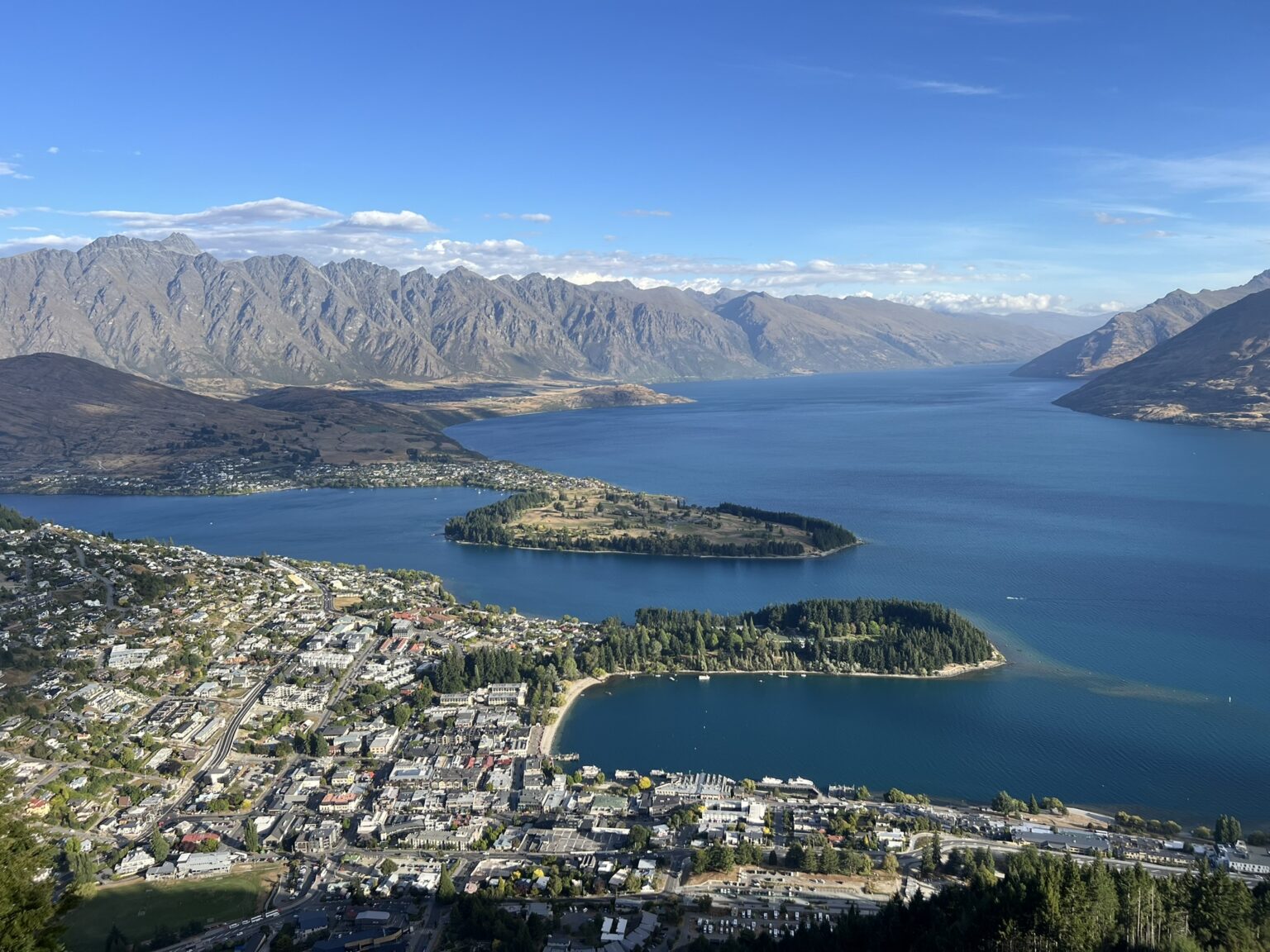 A town sitting on the edge of lake between mountains that can be visiting on your trip to Queenstown