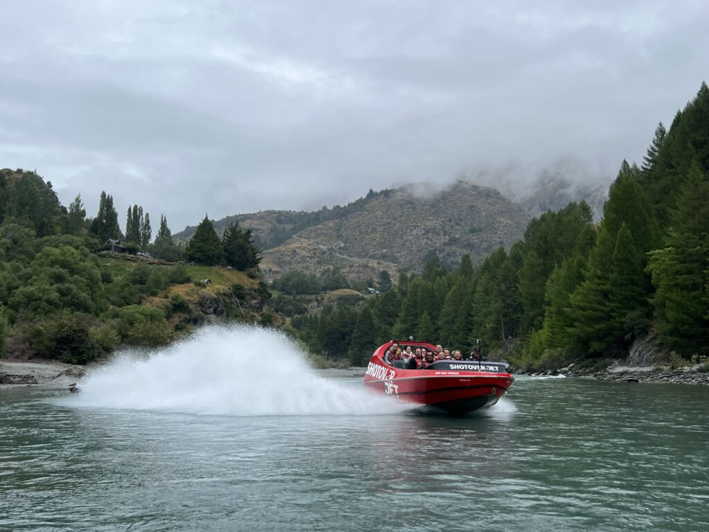 A boat splashing through a river with mountains behind for an activity that can be done when visiting Queenstown