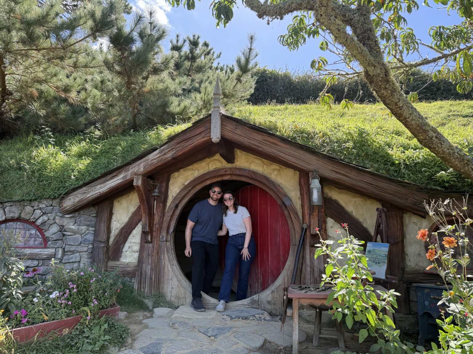 Two people standing in front of a red door to a home built into a hill