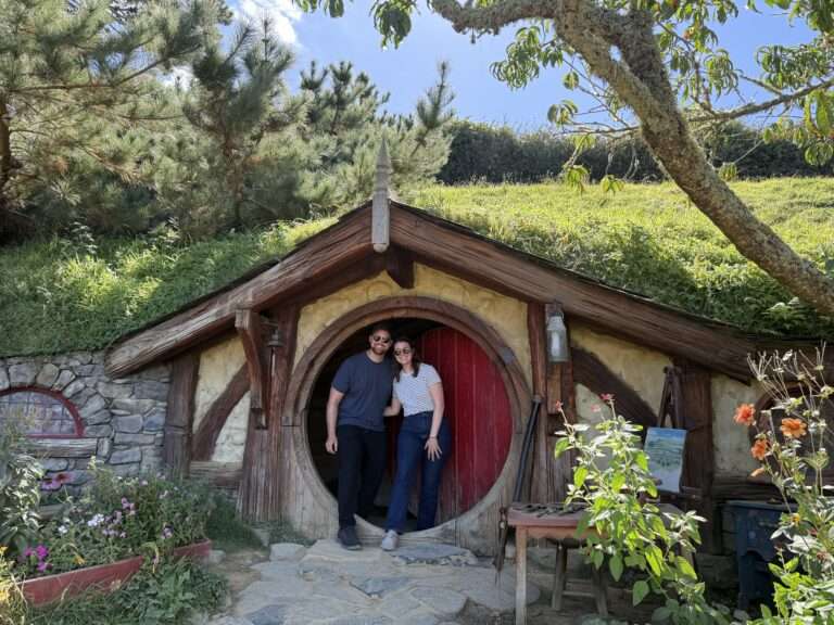 Two people standing in front of a red door to a home built into a hill