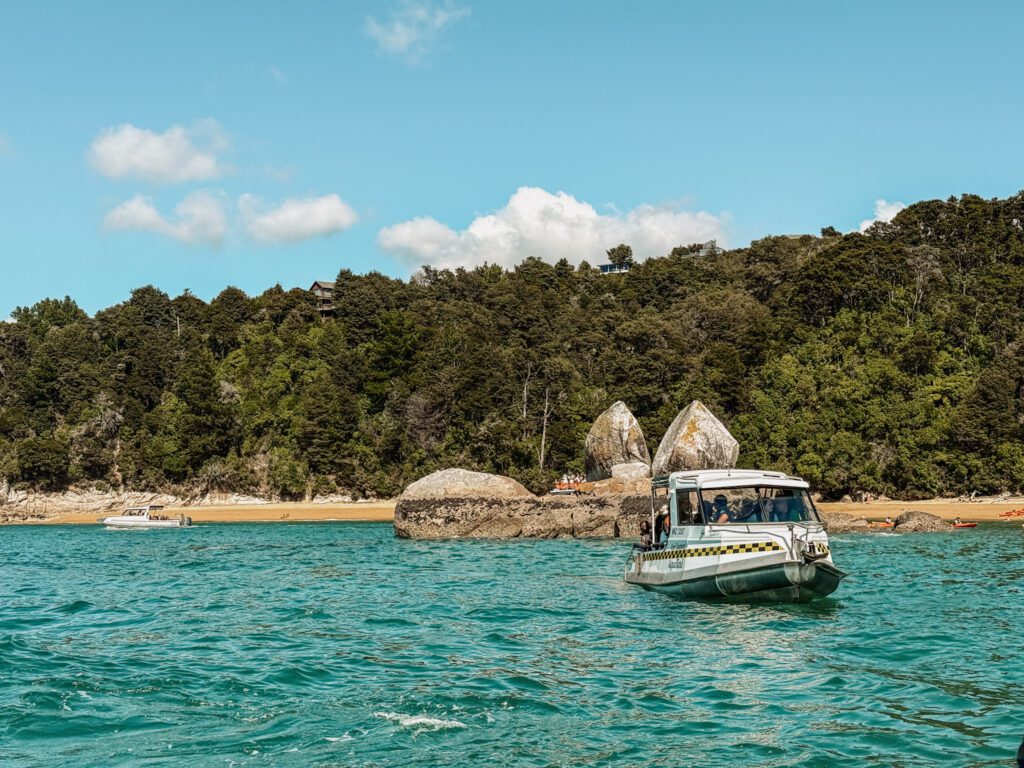 a boat in a bay with a beach and tropical coast in the background in Abel Tasman National Park