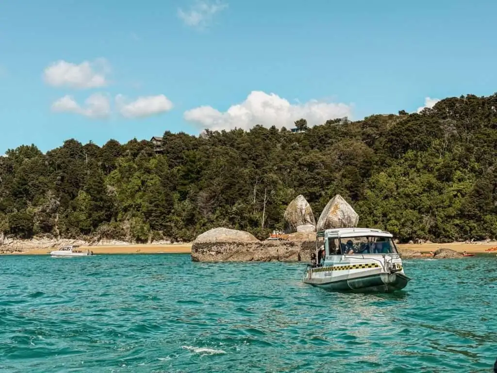 a boat in a bay with a beach and tropical coast in the background - Things to do in Abel Tasman National Park