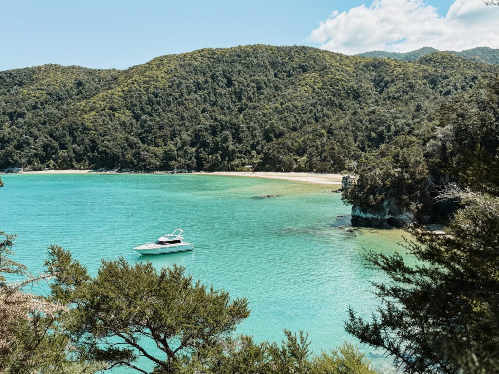 A boat anchored in a bay with turquoise water and surounded by white sand beaches and tropical forests in Abel Tasman National Park
