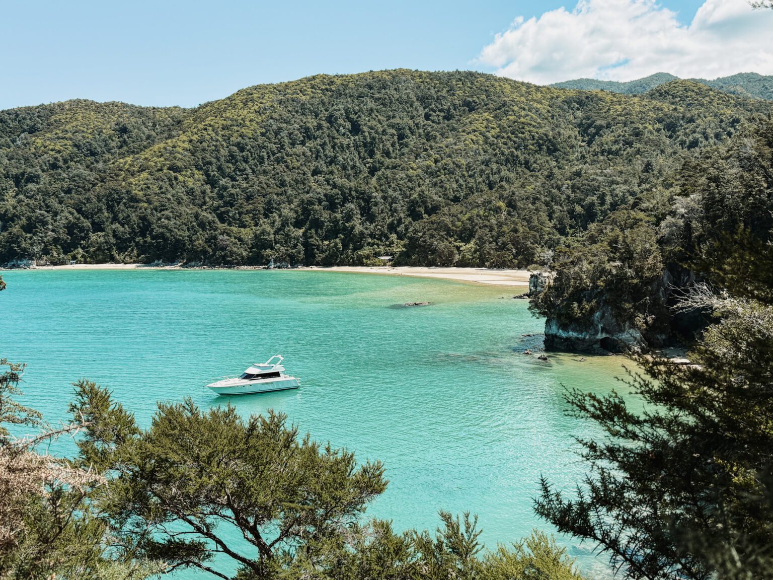 A boat anchored in a bay with turquoise water and surounded by white sand beaches and tropical forests in Abel Tasman National Park