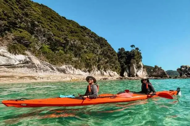Two people in a kayak in turquoise water with a coastline behind them - Things to do in Abel Tasman National Park