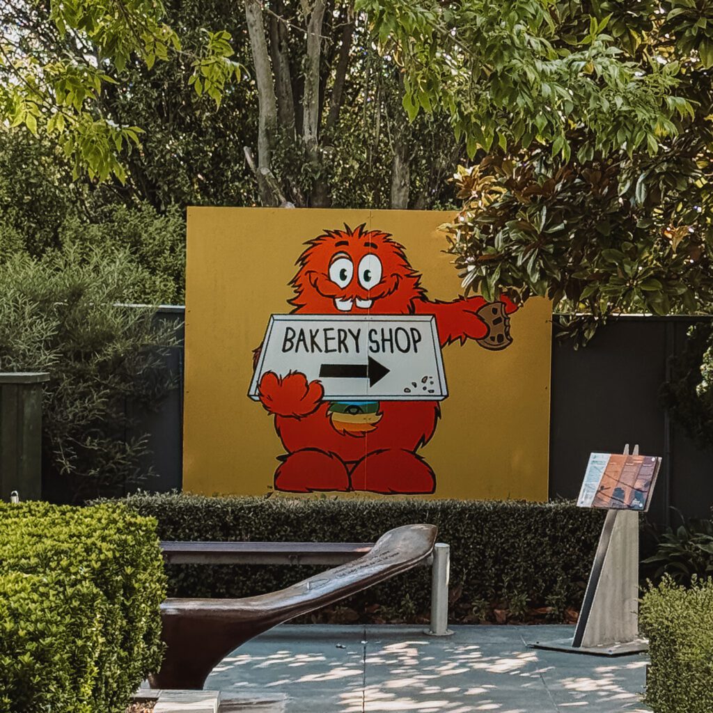 A sign with a red furry character holding a sign pointing to a shop on the Queenstown to Christchurch road trip