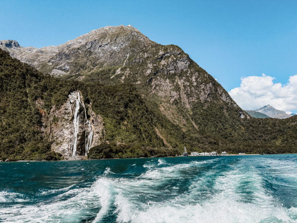 The wake of a boat going through water surrounded by mountains in Fiordland National Park