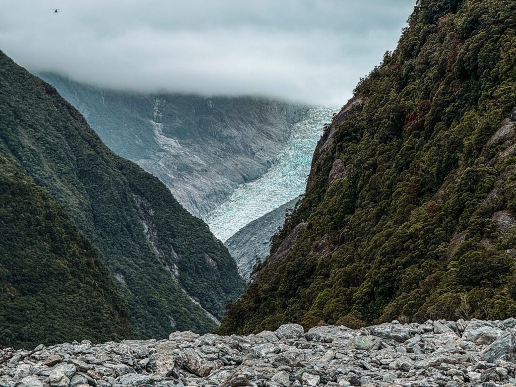 A glacier flowing down a mountain in the distance in the West Coast of New Zealand