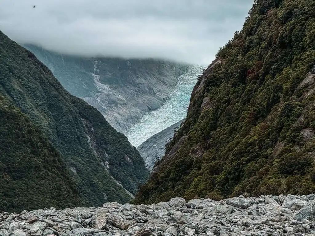 A glacier flowing down a mountain in the distance in the West Coast of New Zealand