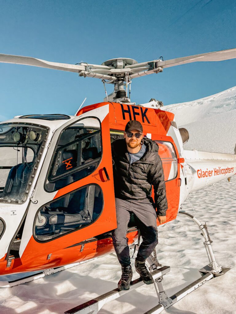 A man hopping out of a helicopter on snow in the West Coast of New Zealand