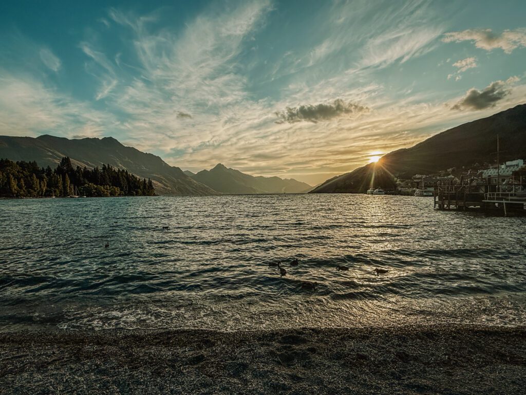 Sun setting over a lake surrounded by mountains to be seen on the Queenstown to Christchurch road trip