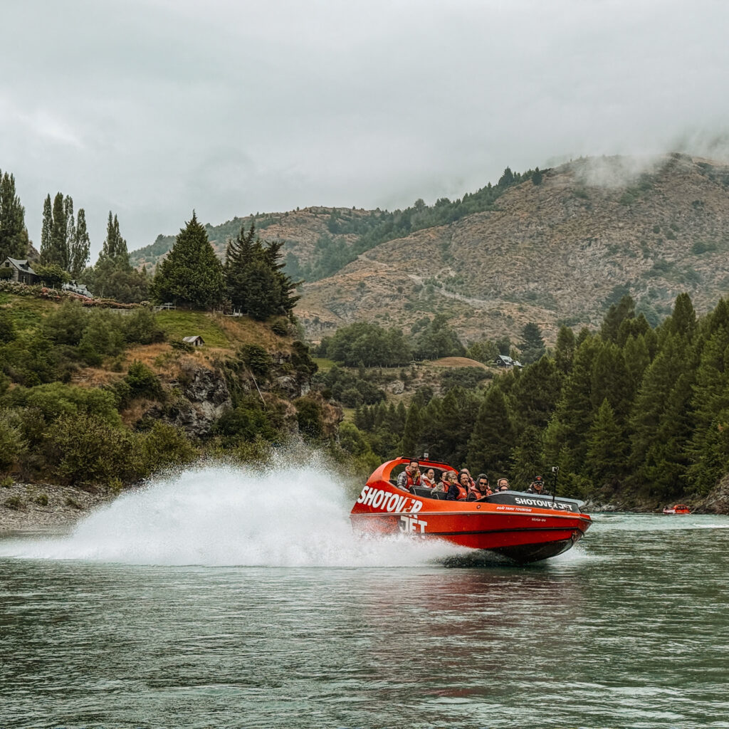 A boat splashing through a river between mountains that can be done between Queenstown and Christchurch