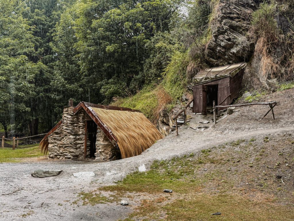 Wooden and thatched buildings in a hillside that can be seen between Queenstown and Christchurch