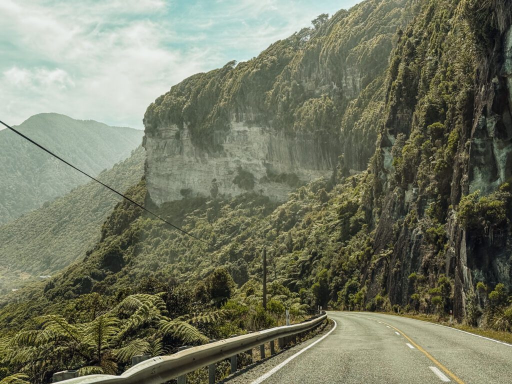 A road winding around a forested cliff on the West Coast of New Zealand