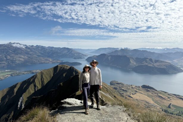 Two people posing on the edge of a mountain overlooking a lake within mountains near the Southern Alps