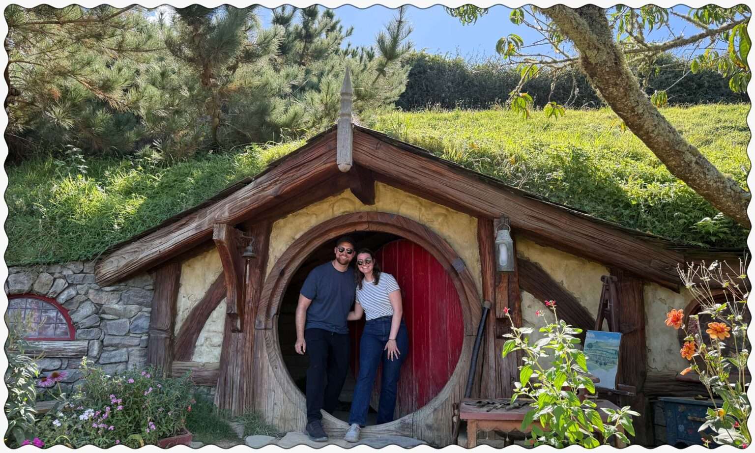 Two people standing in front of a red door to a home built into a hill