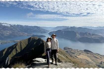 Two people posing on the edge of a mountain overlooking a lake within mountains near the Southern Alps