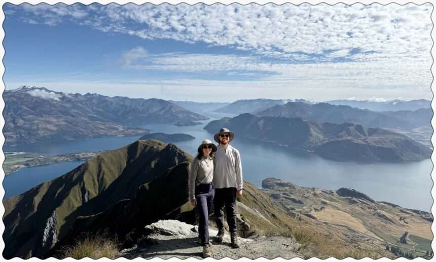 Two people posing on the edge of a mountain overlooking a lake within mountains near the Southern Alps