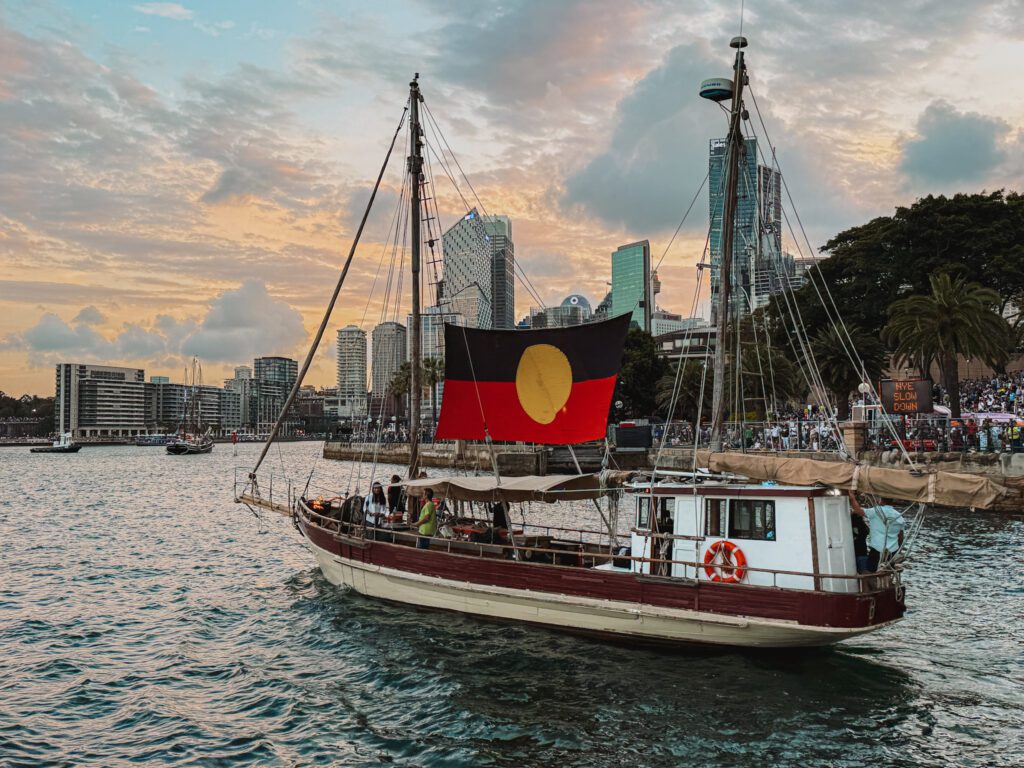 A sailboat holding the Australia Aboriginal flag in the harbor in front of the city skyline on New Year's Eve