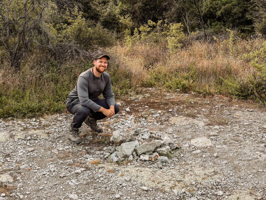 A man crouching in front of a pile of rocks used as one of the filming locations in the Lord of the Rings