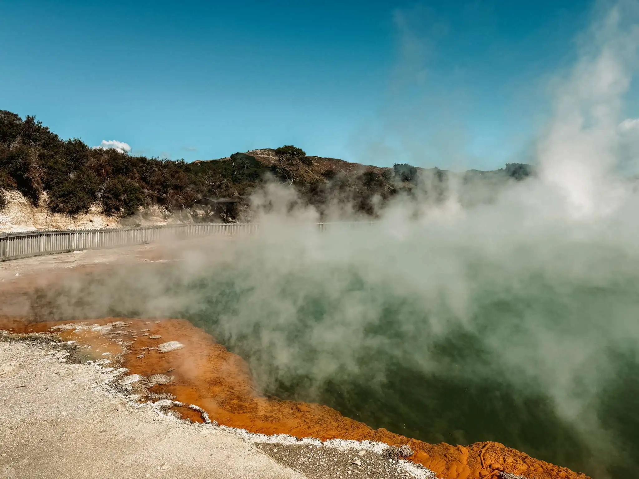 A smoking pool of water with an orange rim as part of a Rotorua Itinerary in the North Island of New Zealand