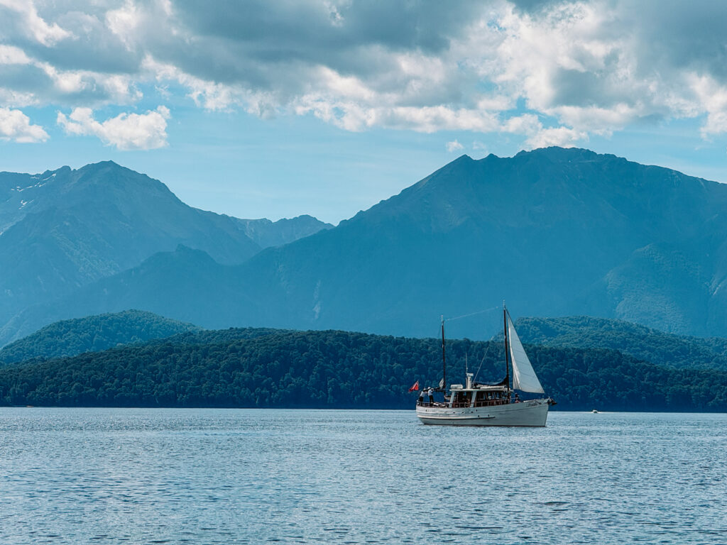 A sailboat on a lake that has one of the best beaches of New Zealand with mountains in the background