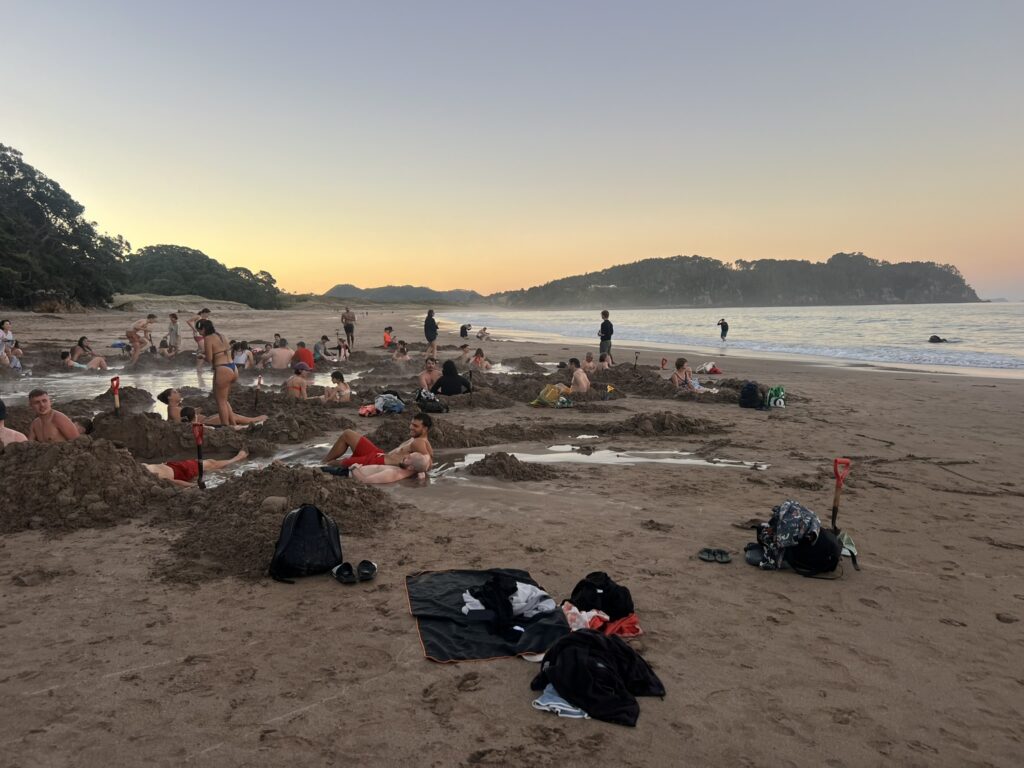 A group of people sitting in puddles of water at the beach of the Coromandel Peninsula