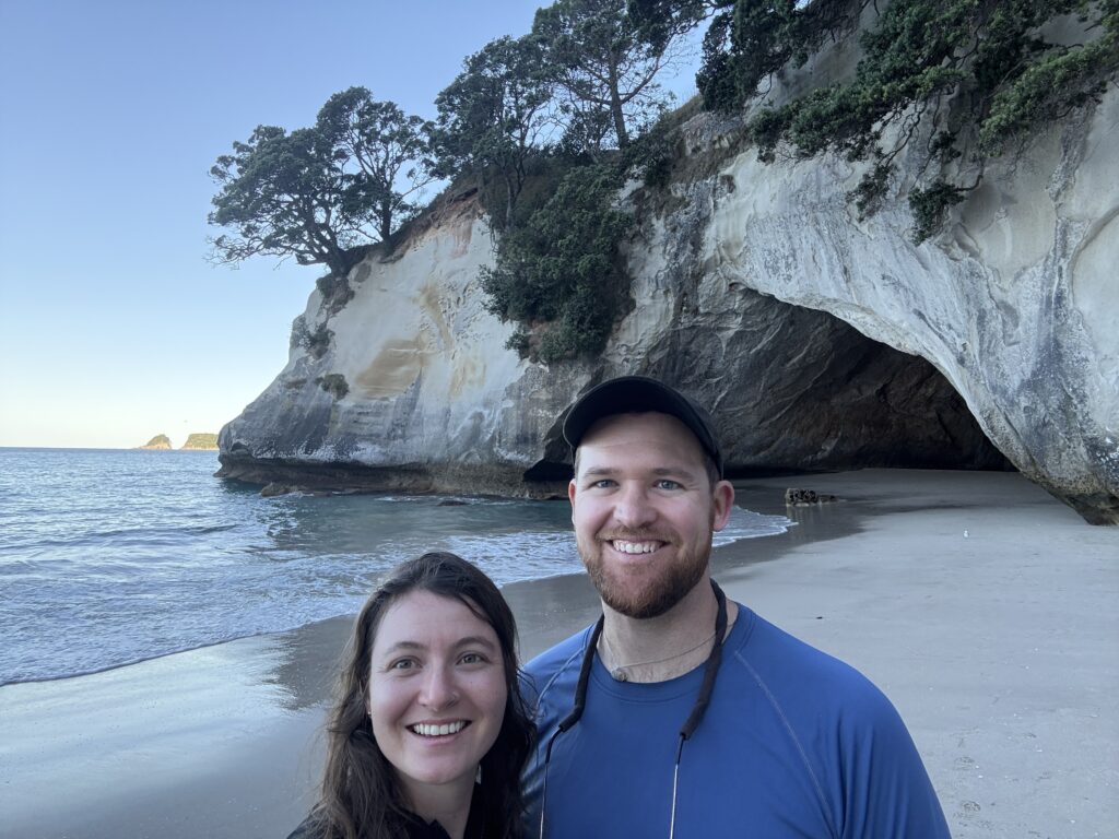 Two people standing in front of a rock arch at a beach in the Coromandel Peninsula