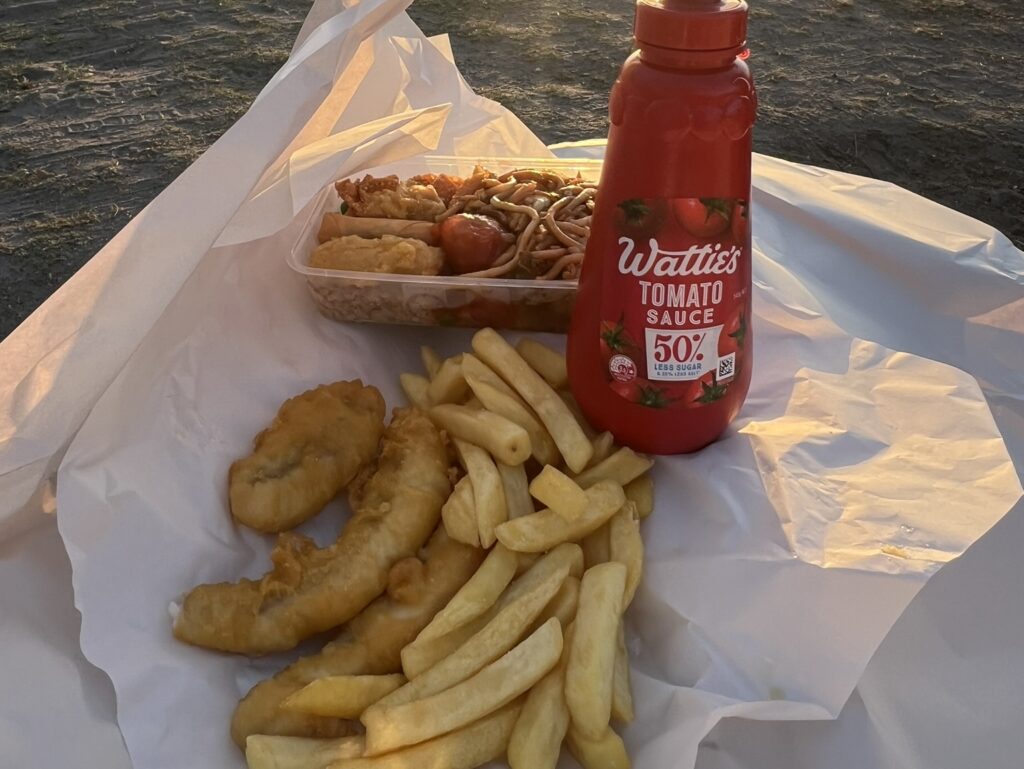 A bottle of ketchup and fried fish, french fries, and a to go container of chinese food to represent some of new zealand food and drinks