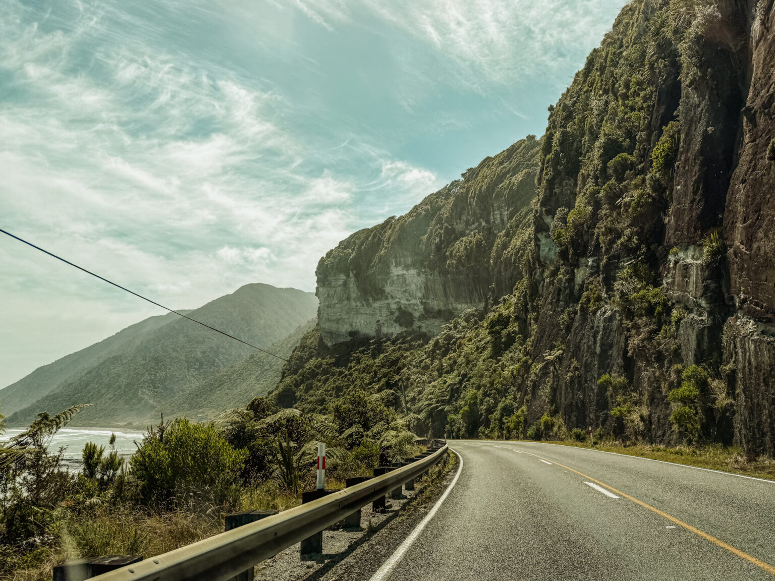 A road along a beautiful coastline full of cliffs and forests and a good example of where you may consider is New Zealand safe when it comes to driving
