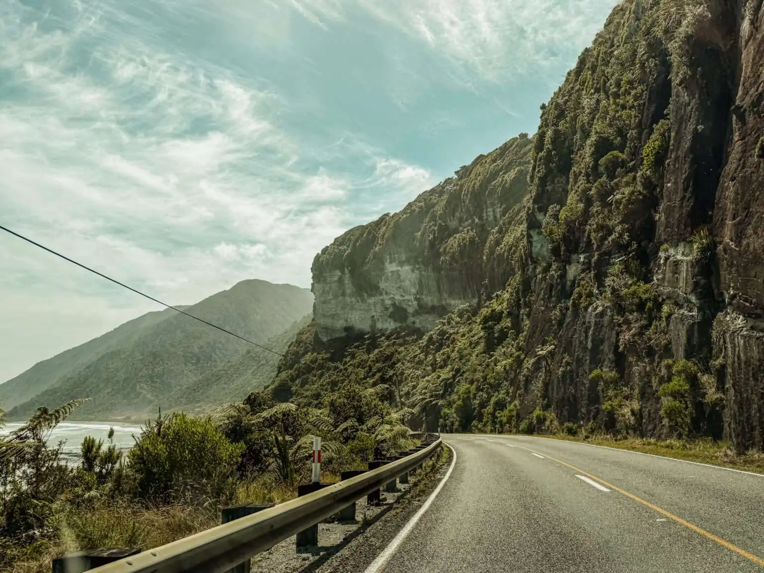A road along a beautiful coastline full of cliffs and forests and a good example of where you may consider is New Zealand safe when it comes to driving