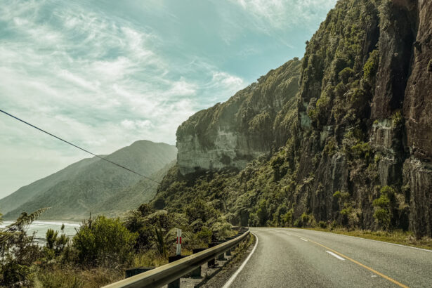 A road along a beautiful coastline full of cliffs and forests and a good example of where you may consider is New Zealand safe when it comes to driving