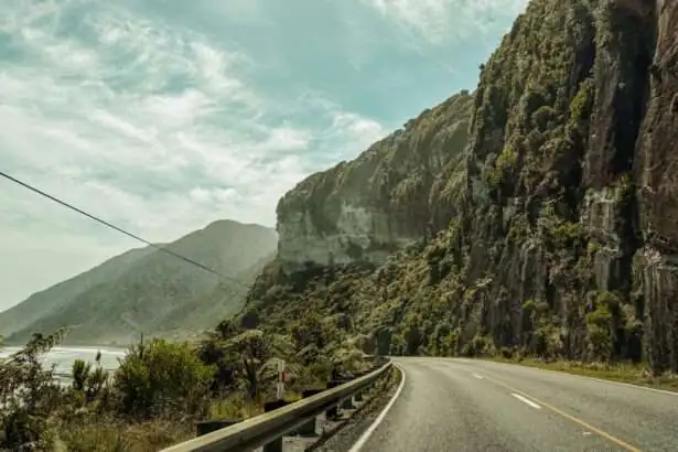 A road along a beautiful coastline full of cliffs and forests and a good example of where you may consider is New Zealand safe when it comes to driving