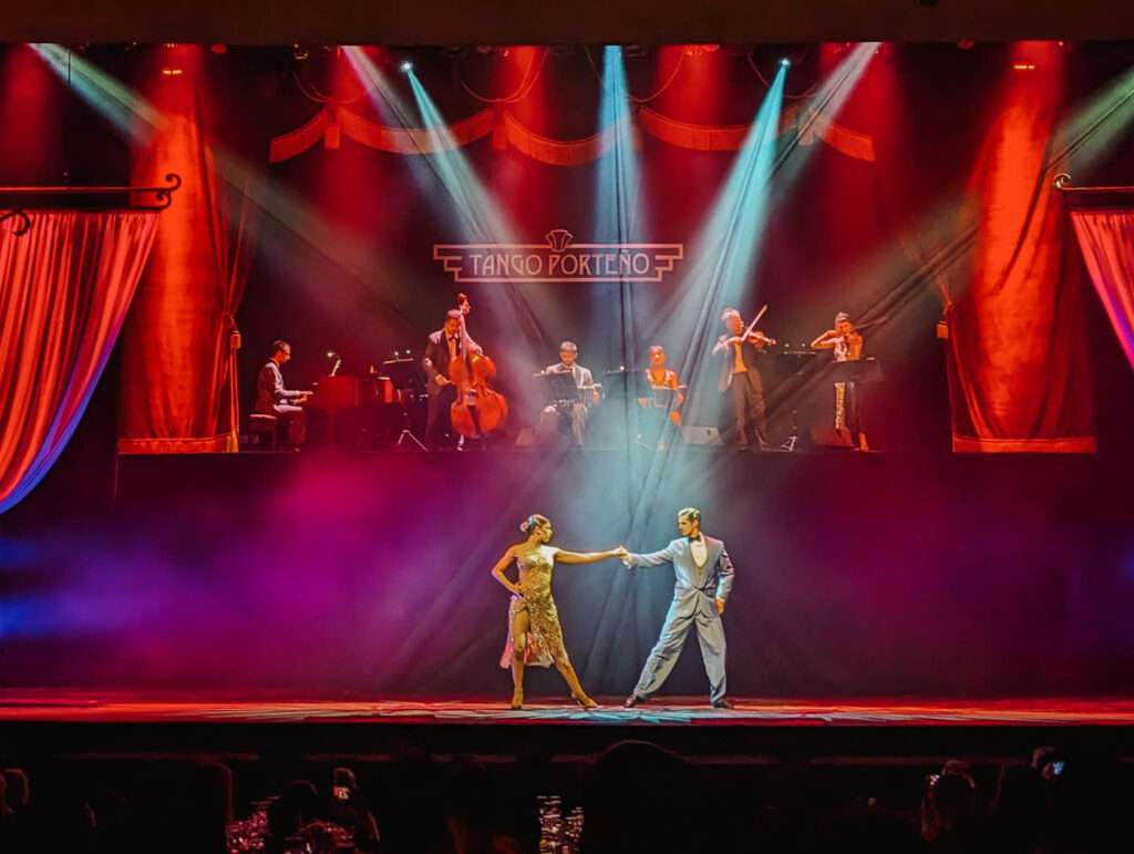 Two tango dancers on stage with a bunch of musicians