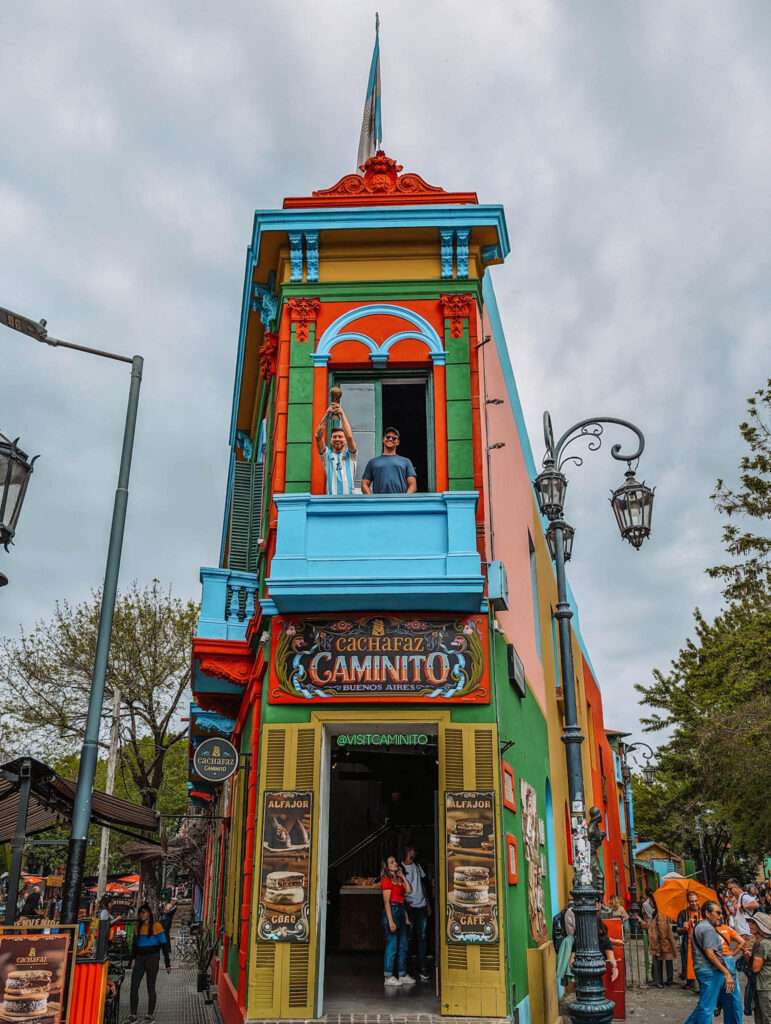 What to do in Buenos Aires - A man standing next to a statue of Messi on the second floor of a colorful building in La Boca