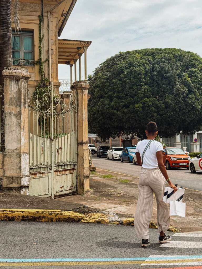 A woman crossing the street towards an old building with a white fence in French Guiana