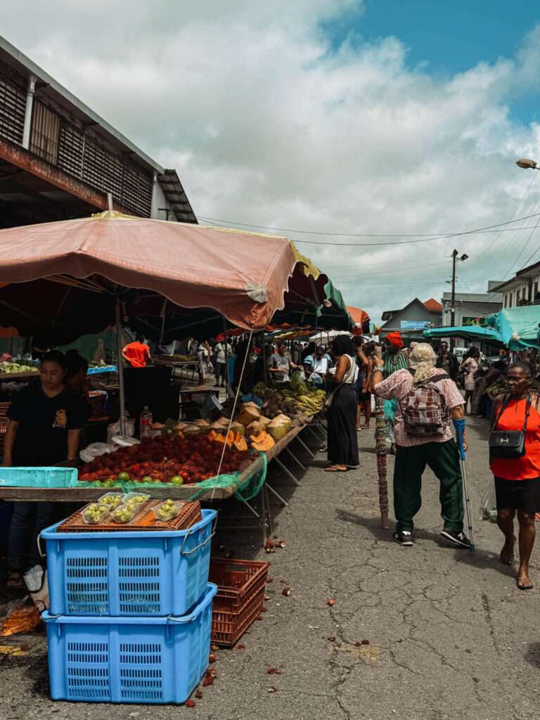 People walking through an outdoor market of produce as one of the things to do in Cayenne