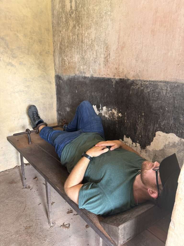 A man laying on a wooden bench in a concrete room in French Guiana
