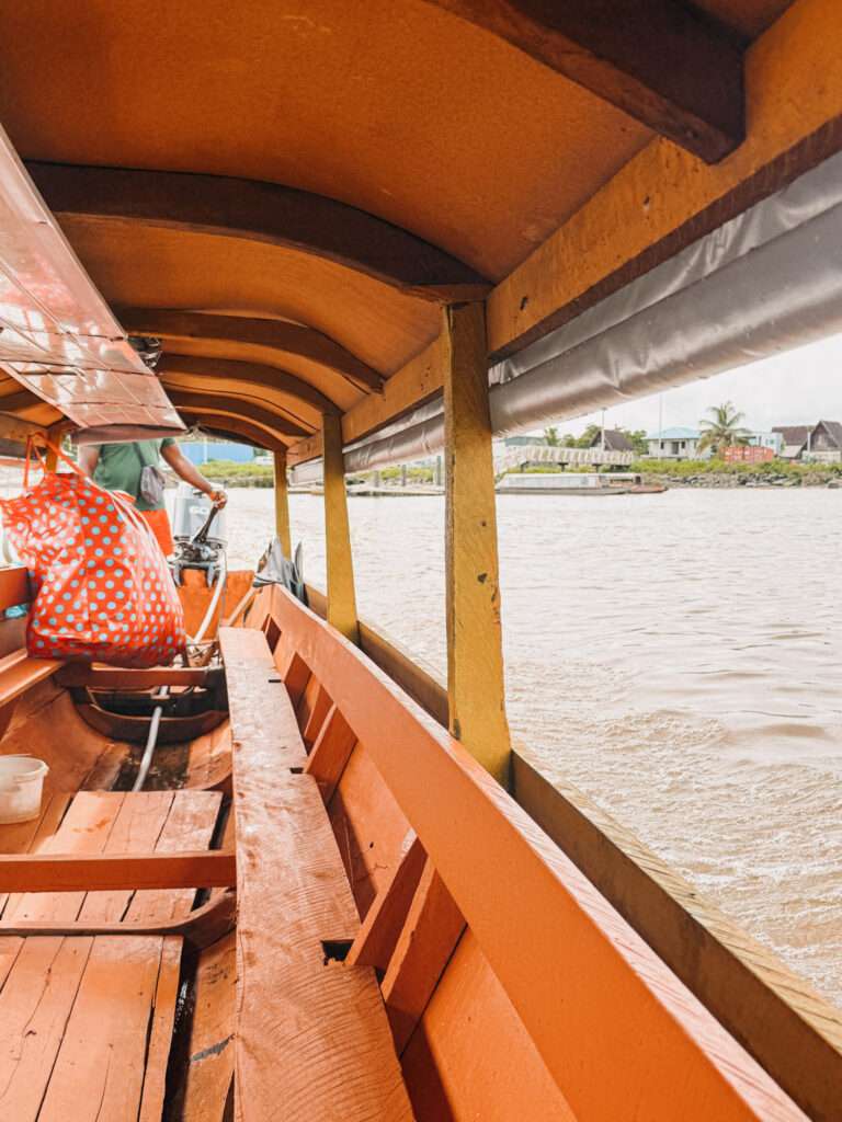 A wooden pirogue with a wooden roof painted orange and going across the river to cross the border between French Guiana and Suriname