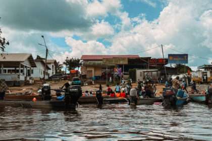 A dock of pirogues on the side of a river with buildings in the background - Guianas Itinerary