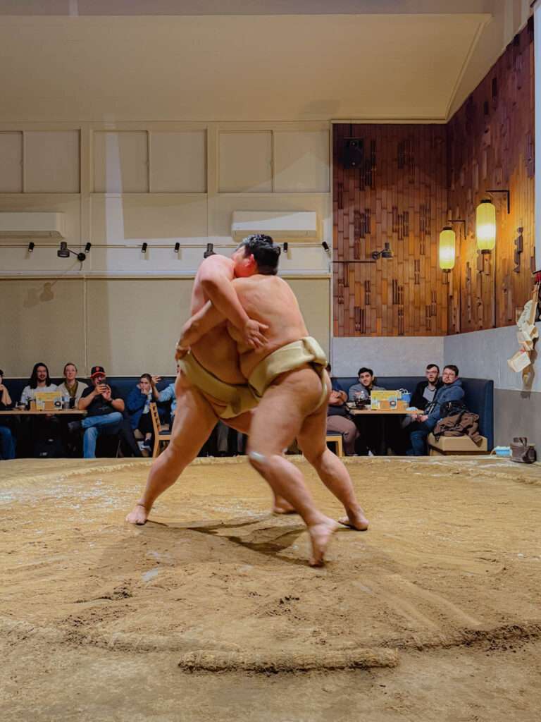 Two sumo wrestlers fighting in a ring during a lunch experience in Tokyo
