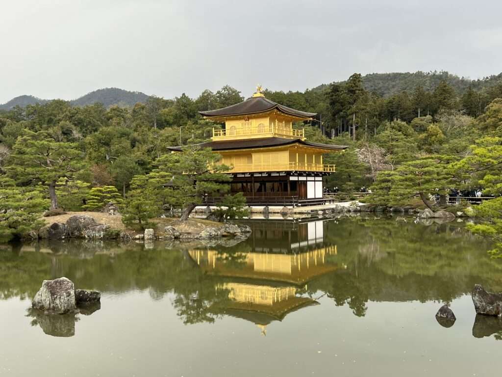 A temple that is covered in gold leaf at the edge of a large pond in the forest