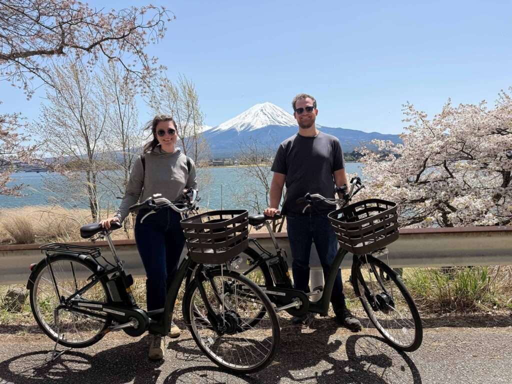 Two people on bikes in front of a lake with Mount Fuji behind