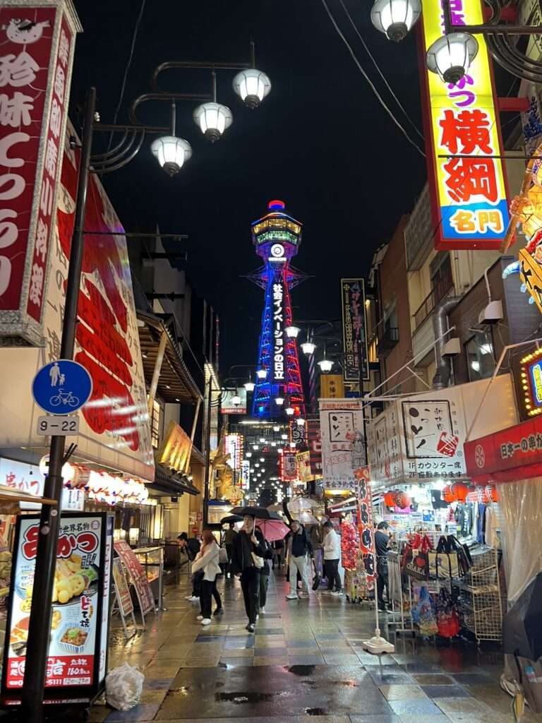 The lit up pedestrian street of Osaka lined with shops in the rain