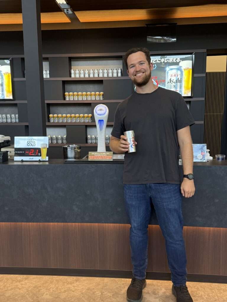 A man holding a beer in front of a draft pour at the Asahi brewery of Osaka, Japan
