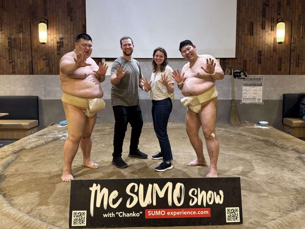 Two sumo wrestlers and people standing in a sumo wrestling ring
