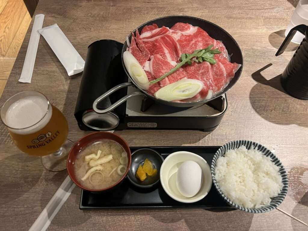 A dish of raw meat and veggies over a burner with some sides